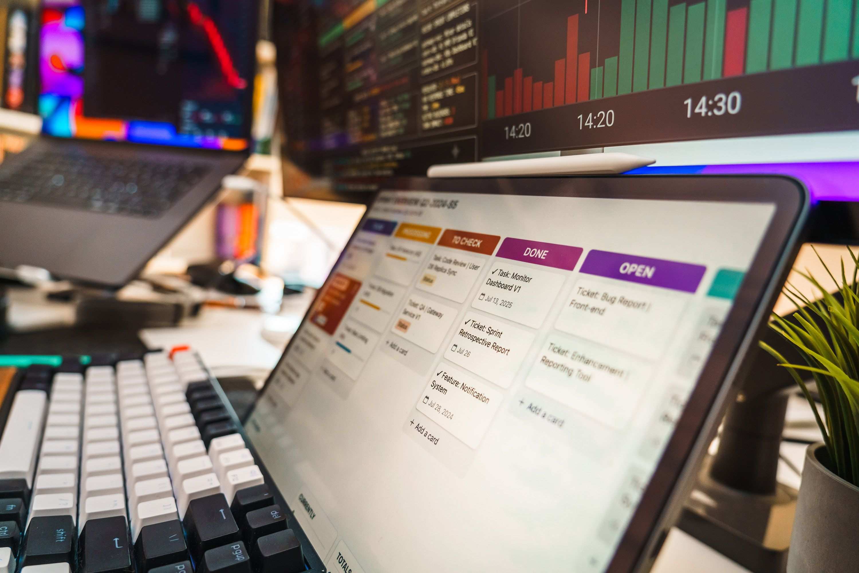 Arbeitsplatz mit Laptop und Unterlagen in einem Büro, Monitore mit Datencharts